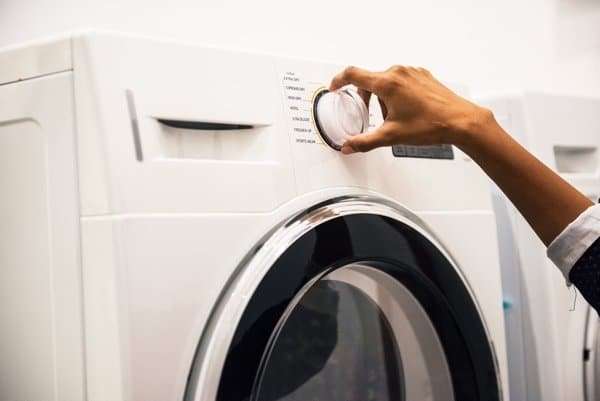 Person adjusting washing machine dial – front-loading washing machine ready for repair or installation.